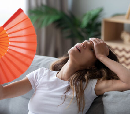 Overheated,Woman,Sitting,On,Couch,,Waving,Orange,Paper,Fan,Close