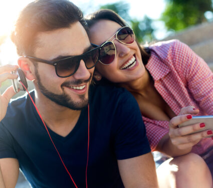 Portrait,Of,Two,Friends,Using,Mobile,Phone,And,Listening,To