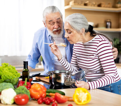 Beautiful,Senior,Woman,Tasting,Food,While,Cooking,With,Husband,In